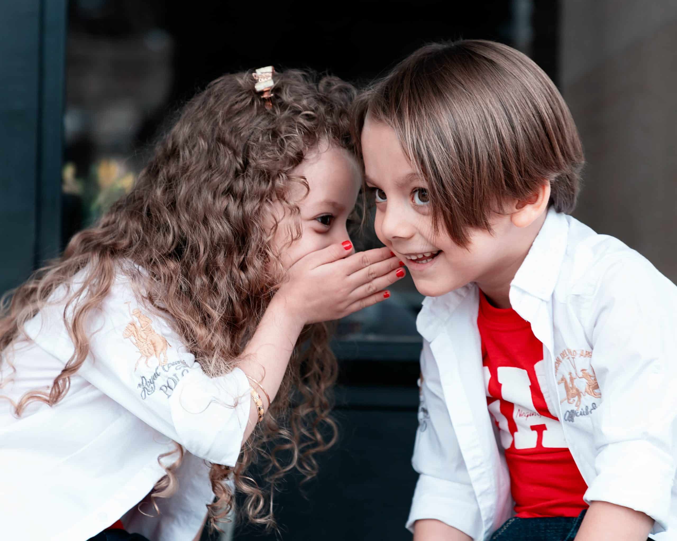 Little girl leaning over to whisper something to a little boy