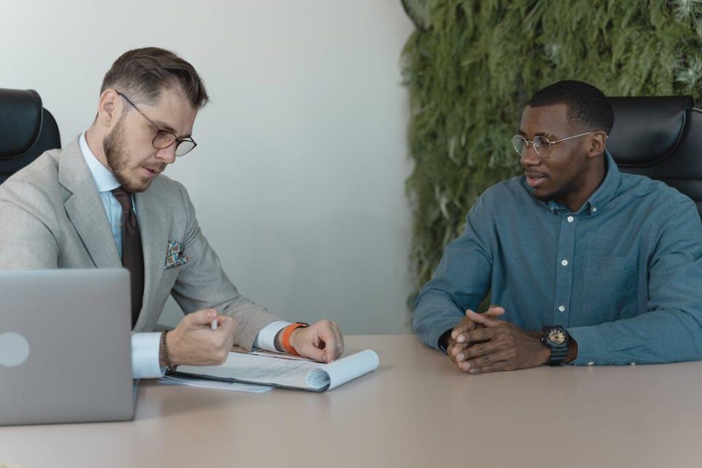 Two men at an office table review a resume.